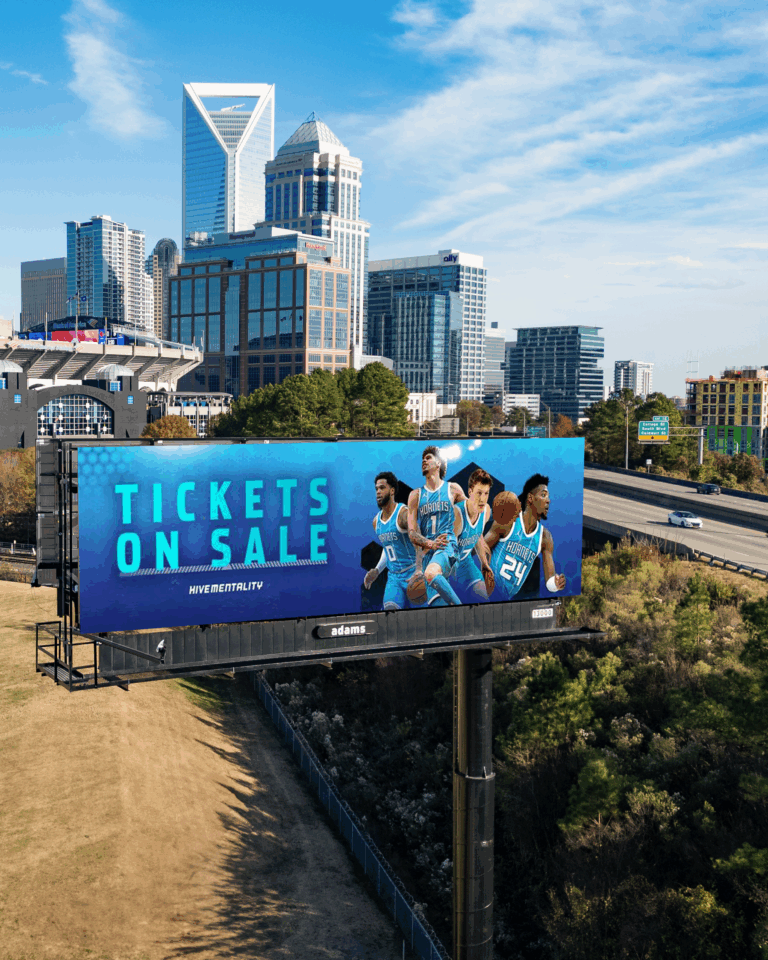 Stand-alone billboard near a major interstate in downtown Charlotte displaying a Charlotte Hornets advertisement, with the city skyline visible in the background