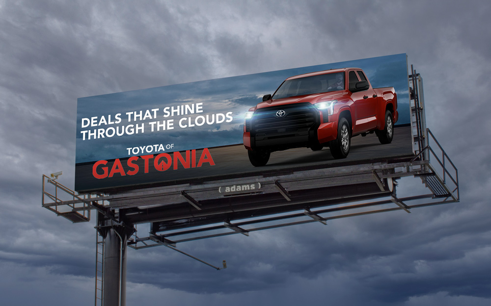 Billboard advertising Toyota of Gastonia featuring a red truck against a cloudy sky with the text 'Deals That Shine Through the Clouds.'
