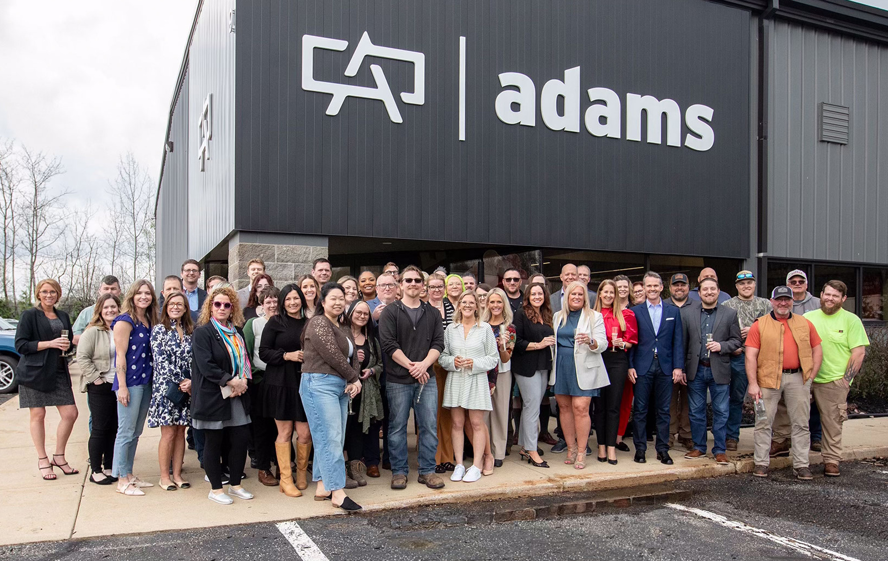 Adams Outdoor Michigan team celebrating new Kalamazoo, Michigan billboard advertising office in front of Adams Outdoor logo.