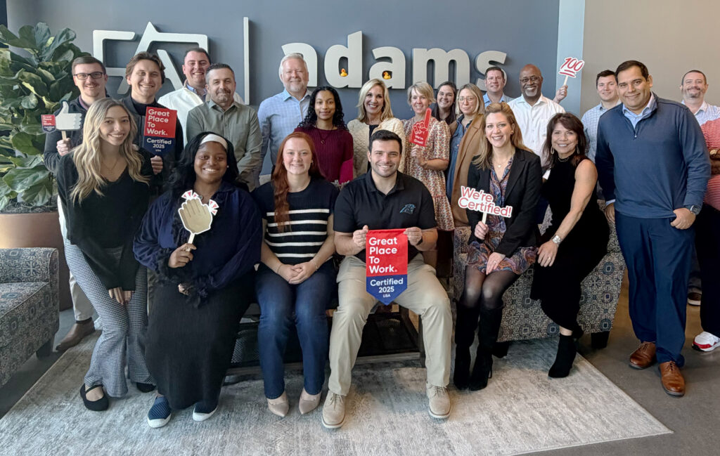 Adams Outdoor Charlotte team posing in front of the Adams logo wall with Great Place To Work Certified 2025 signs and props